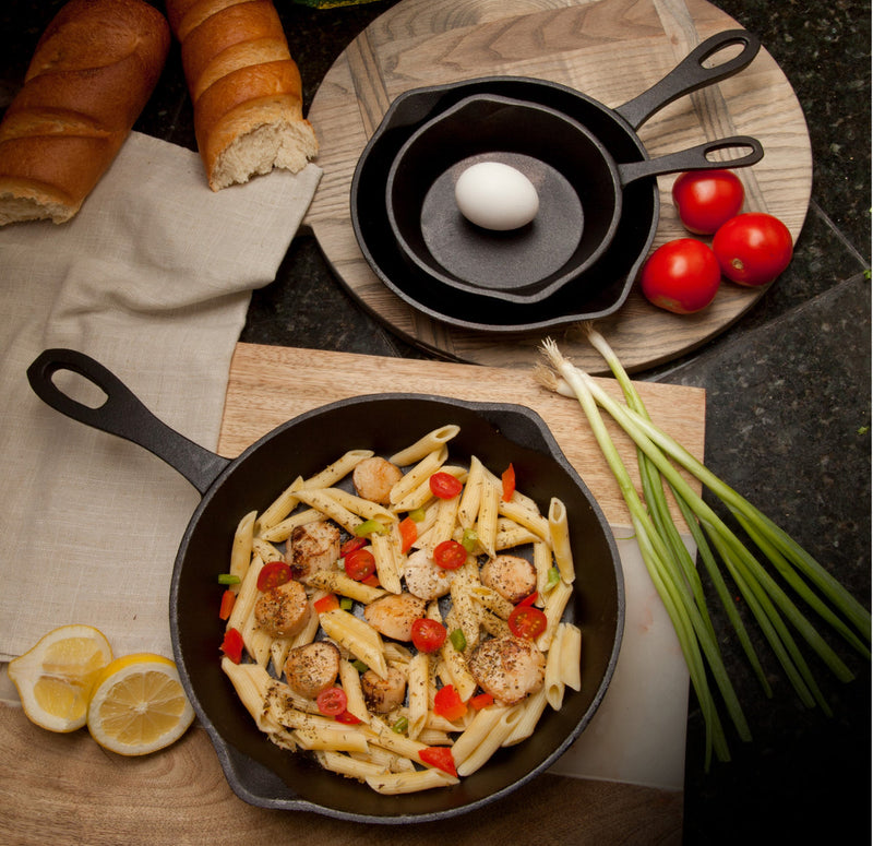 Pasta dish with vegetables and chicken in a cast iron skillet on a wooden surface with bread and tomatoes.