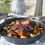 Roasted chickens with vegetables in a black cast iron skillet on a table outdoors.