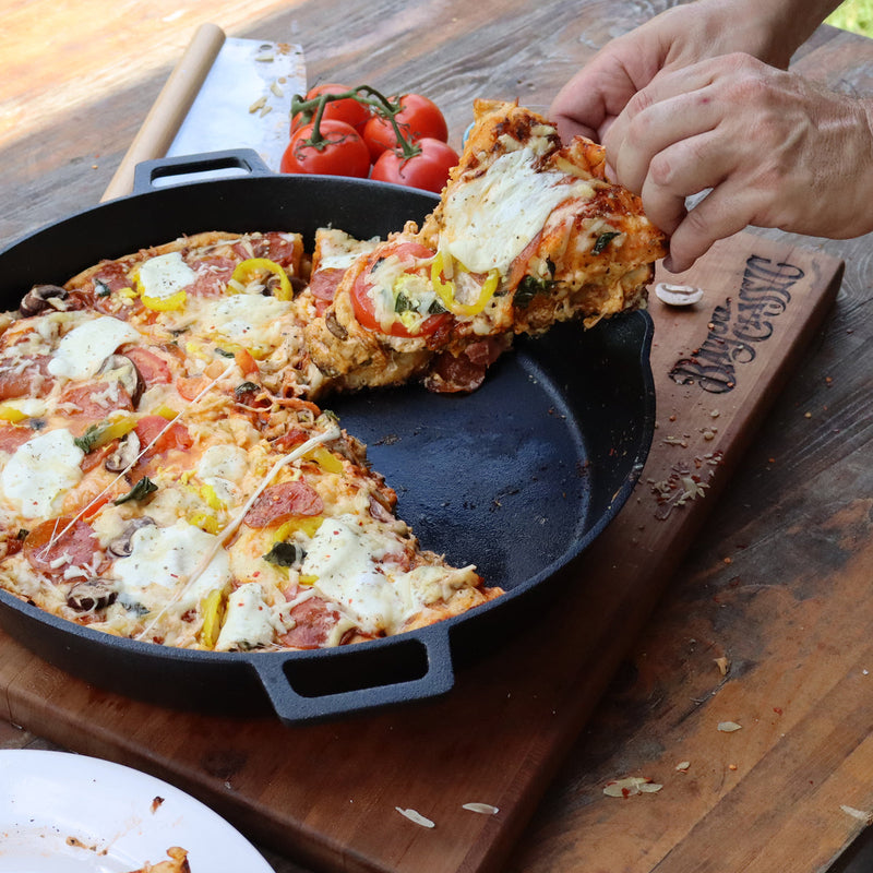 Person taking a slice of pizza from a cast iron skillet on a wooden surface