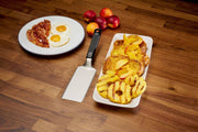 Breakfast setting with eggs, bacon, and grilled pineapple on a wooden table.