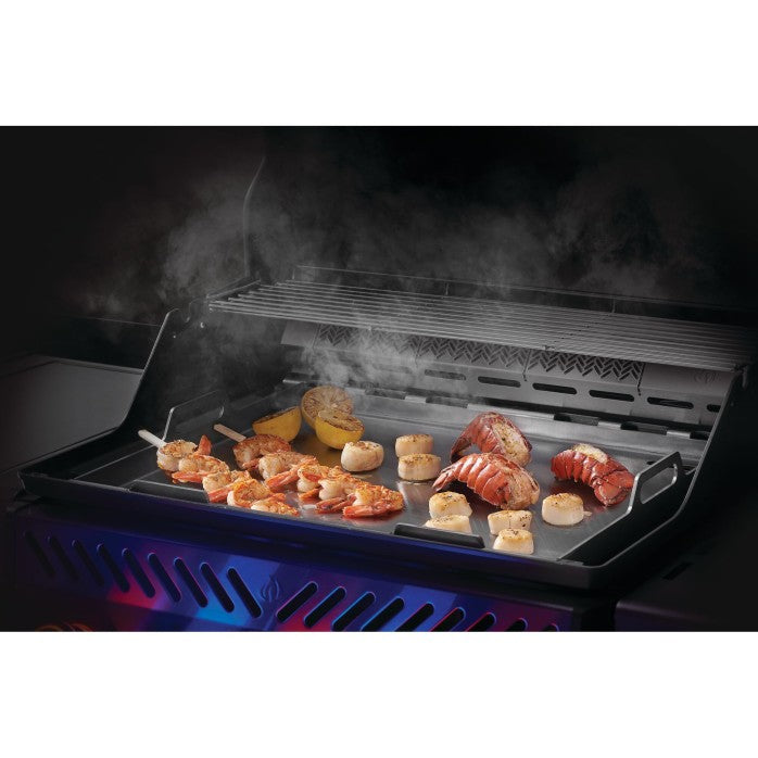 Grill with food being cooked, including shrimp and vegetables, with smoke rising.