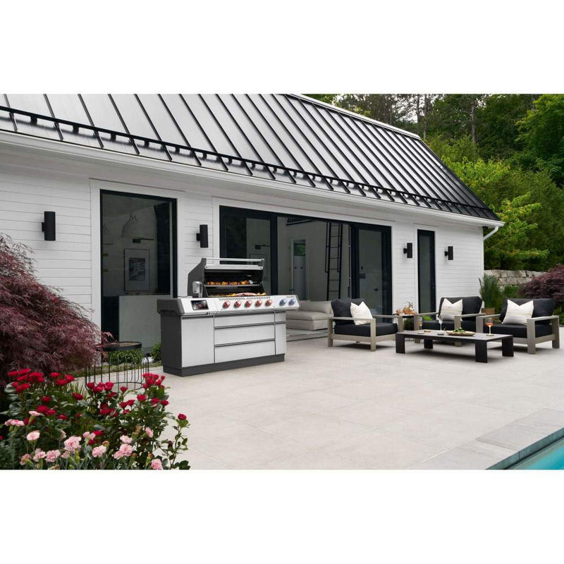 Outdoor patio area with a barbecue grill, seating, and flowers in front of a house.