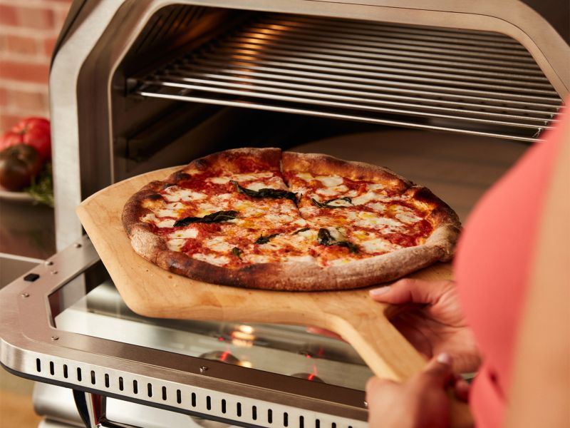 Person placing a pizza into an open pizza oven.